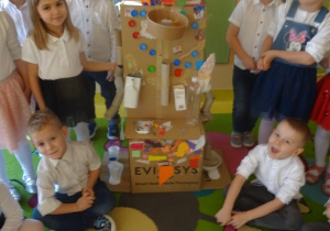 Grupa dzieci stoi wokół przygotowanego robota z kartonów.